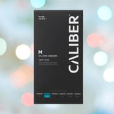 The image displays a black box of Caliber M - Standard Size Condoms (53mm wide), labeled "Made to Fit" and "M" size, containing 12 latex condoms for contraception and STI protection. The backdrop features blurry, circular, multicolored light spots.
